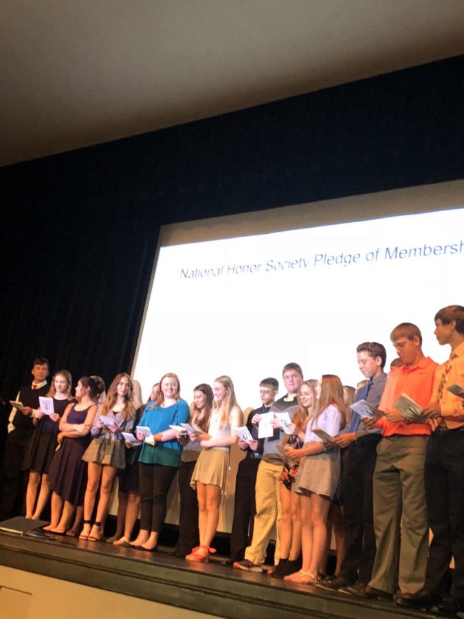 New NHS members take stand on the auditorium stage taking the pledge of membership.