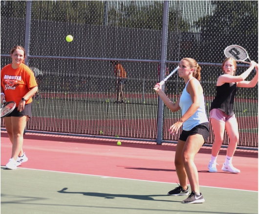 Junior Maddy Muhlig prepares to hit the tennis ball while sophomore Madeline Natvig and junior Taylor Curry watch and wait for their turn on the court. The first tennis practice of the season was held August 19.