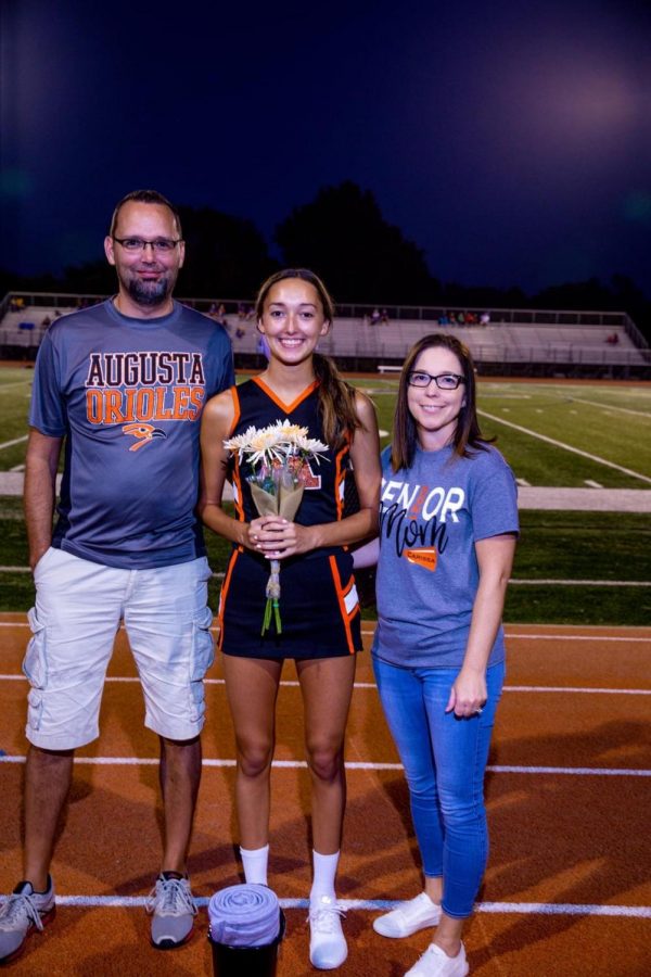 Senior Carissa Mattson stands with her parents after being announced during halftime for senior night. Mattson’s biggest accomplishment in cheerleading is winning the state championship and working hard to progress her skills as a flyer.
