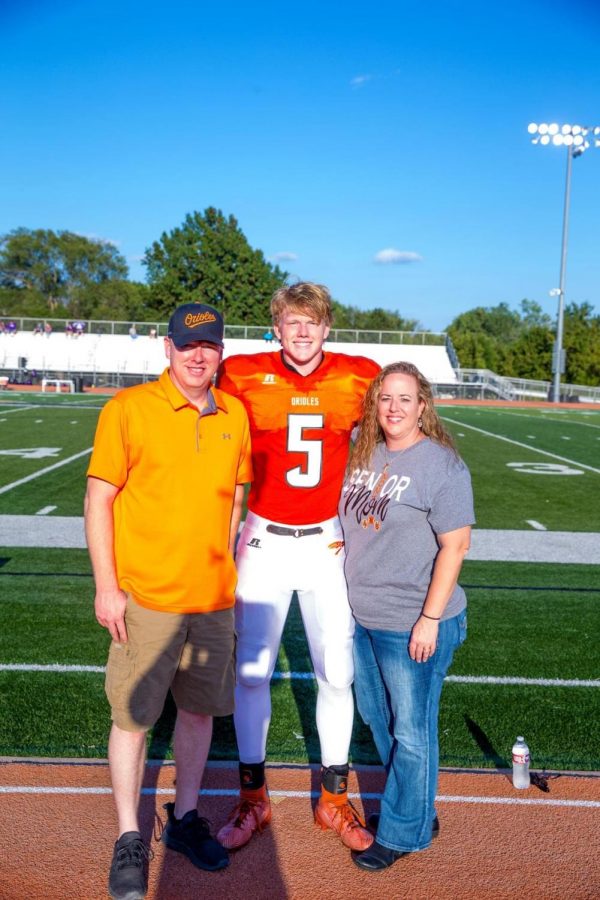 Senior Ely Wilcox stands with his parents on the track at Hillier Stadium after his name was announced. Senior night for football, cheerleading, dance, cross country, and golf was Friday, Sept. 4.