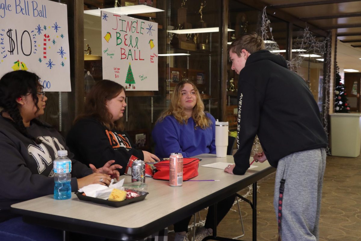 Junior Paul Birk buys a ticket for JBB as senior Abby Marteney hands him his ticket. Senior Jacqueline Macias, and sophomore Annabella Evans volunteer at the table. The dance will be held Dec. 14 at 8p.m. in the commons.