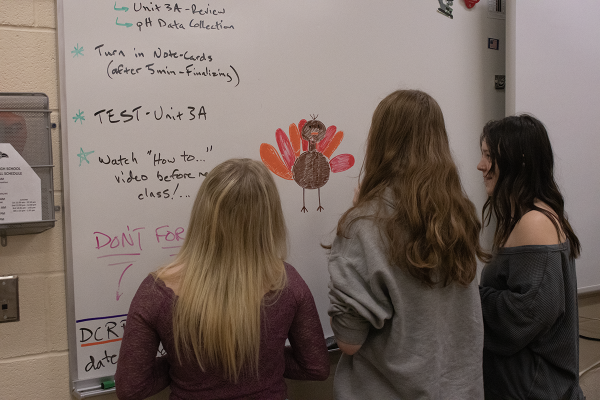 Sophomore Lilly Ullom and juniors Tomasiena Jamis and Skylee Keyser draw a turkey on the board for Thanksgiving. Biology teacher Nathan Stevens was excited about the new change in the schedule.
