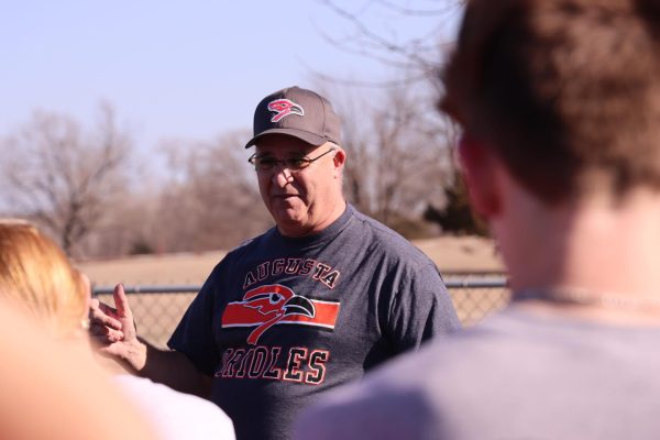 Coach Jeff Regier speaks to the relay runners on passing the baton in a relay race. Track students were stretching during his announcement.
