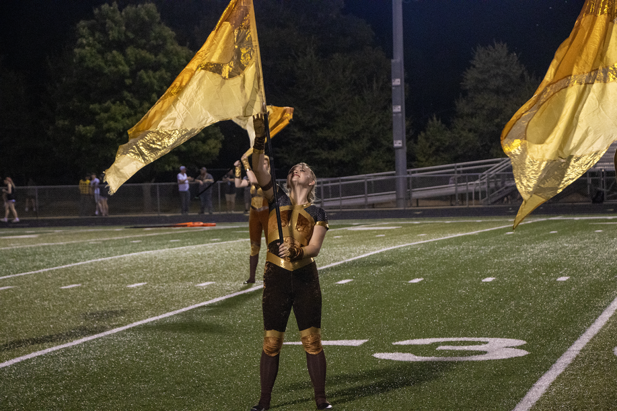 Sophomore Patty Rush raises her flag as an ending to the color guard choreography. Color guard based their outfits on the theme of the marching band show.
